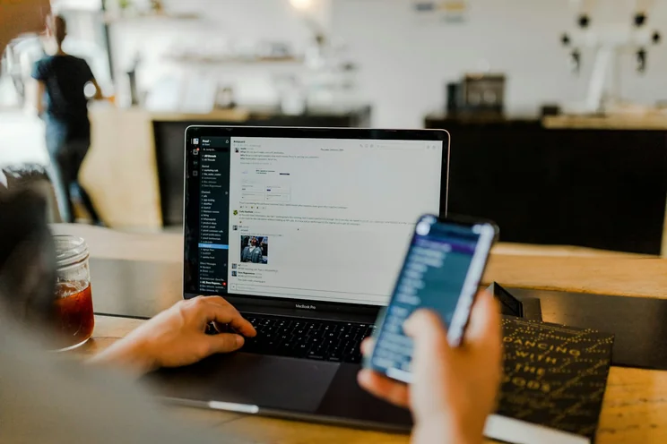 Person nutzt Smartphone und Laptop für die digitale Zusammenarbeit
